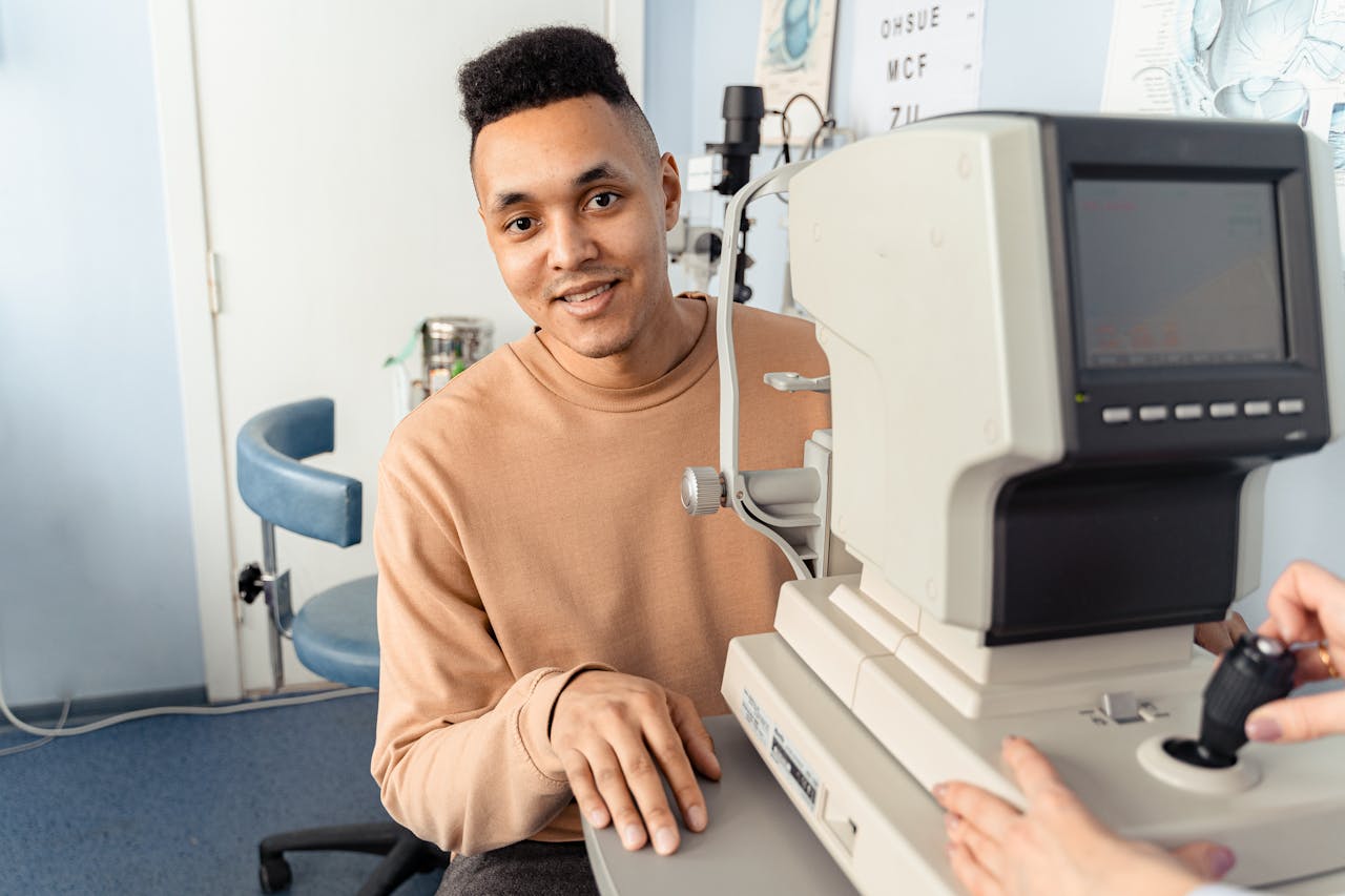 A man happily undergoes an eye examination with an autorefractor inside a clinic setting.